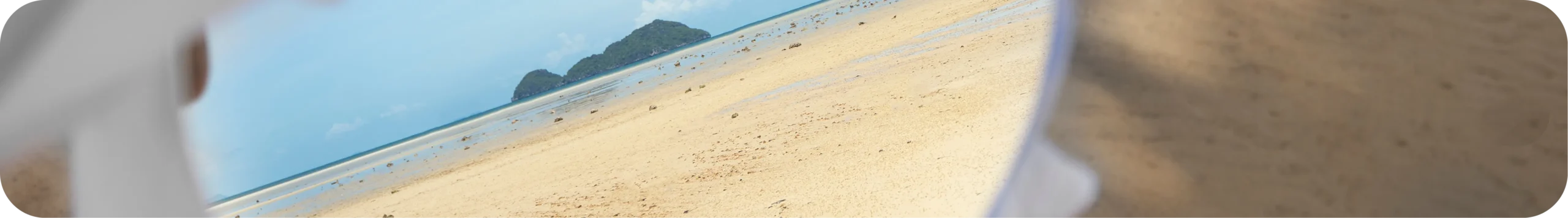 Persona sosteniendo un espejo que refleja una playa y el horizonte